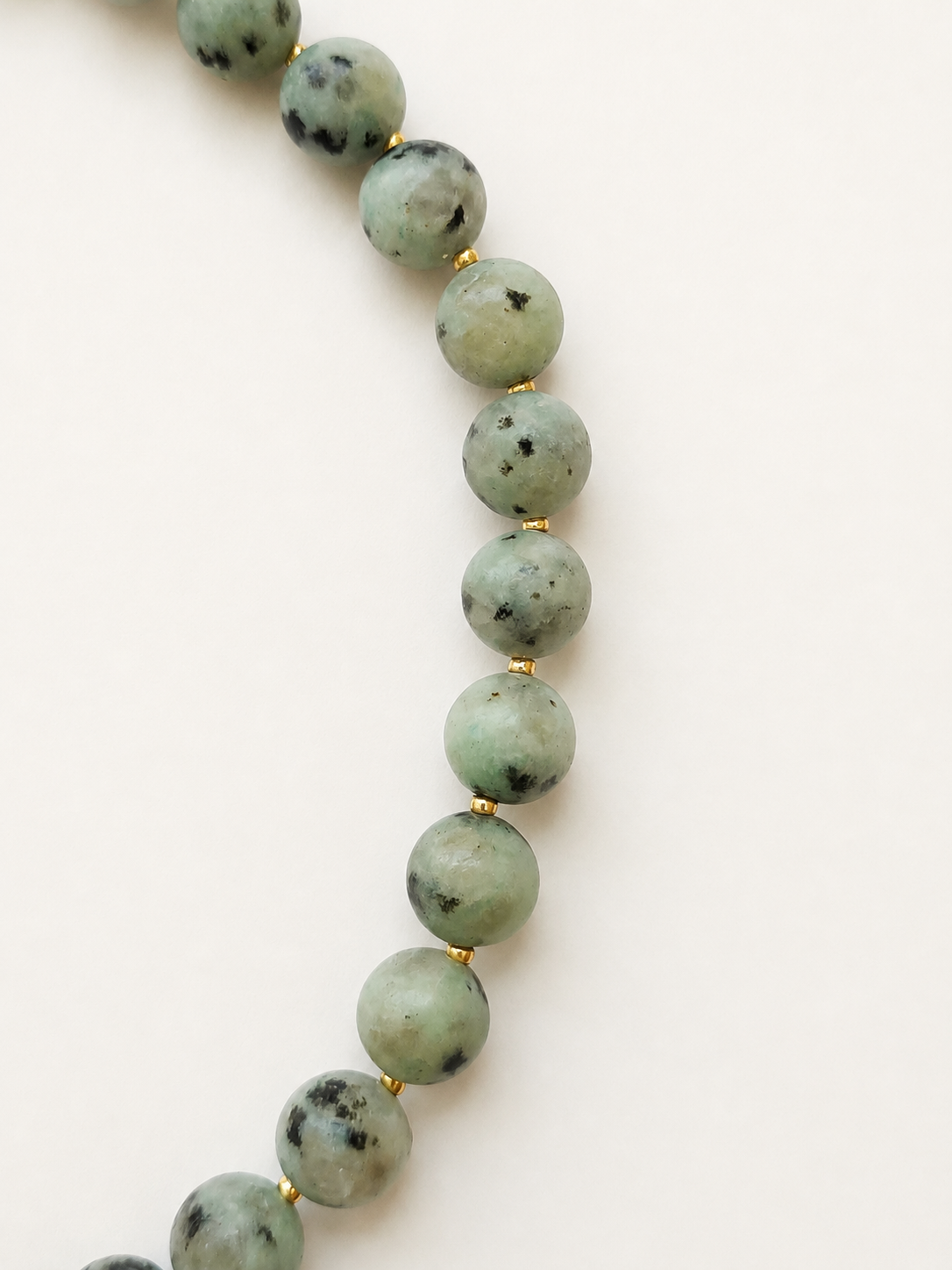 Close-up of pale green kiwi jasper beads with black natural markings and gold Miyuki spacers