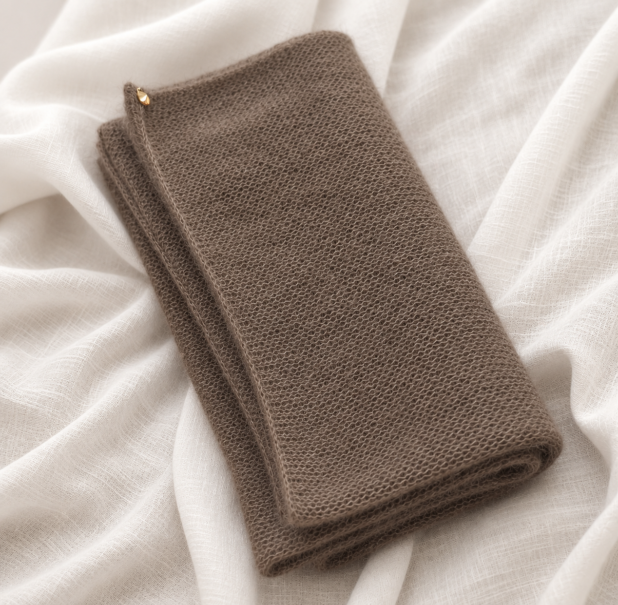 Folded taupe infinity scarf displayed on white linen fabric.