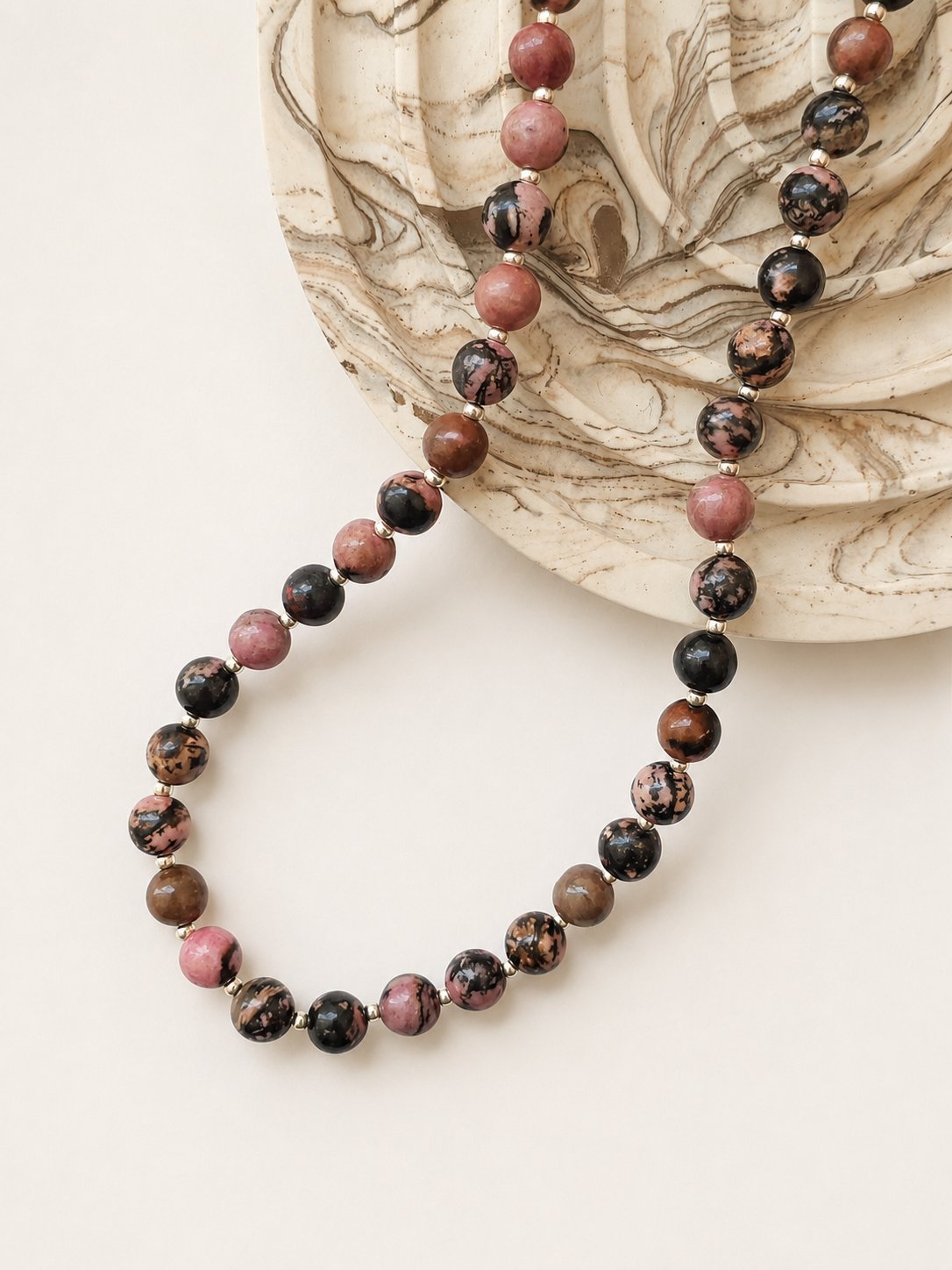 Rhodonite gemstone necklace styled beside a neutral marbled decorative object