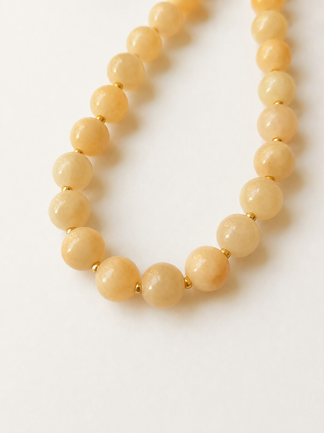 Close-up of creamy peach jadeite beads separated by gold Miyuki accents