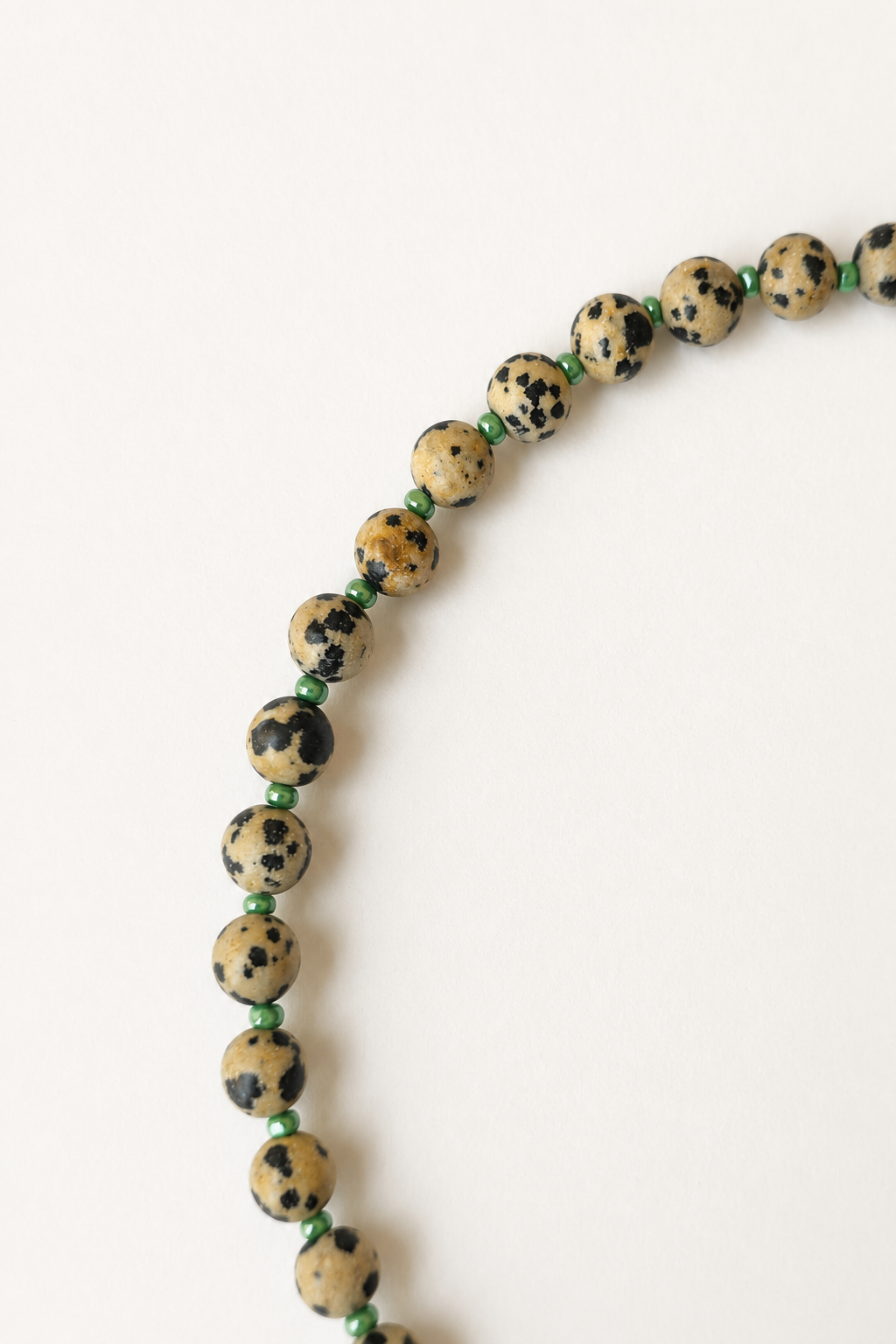 Close-up of 6mm Dalmatian jasper beads separated by glossy green seed bead accent